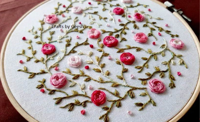 Hand embroidered rose vine using wagon wheel stitch on linen fabric.