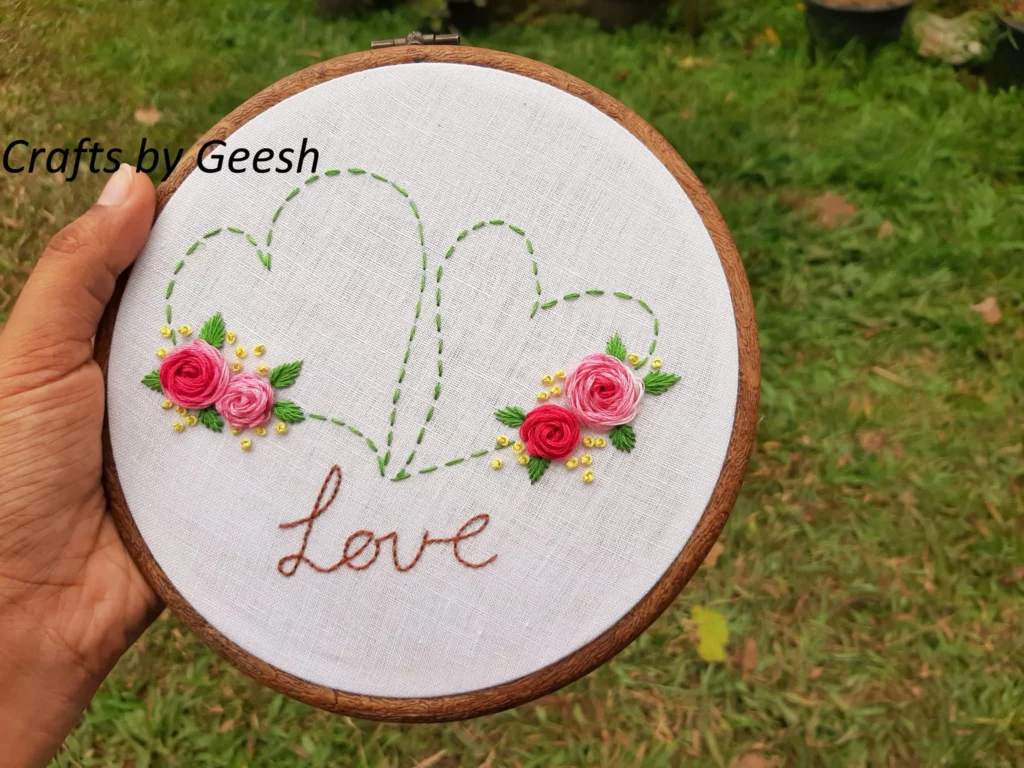 Close up of the word 'LOVE' being monogrammed in hand embroidery using tiny red back stitches.