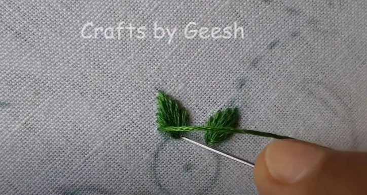 Close up of green leaves being stitched with centered satin stitch on linen fabric for a heart-shaped design.